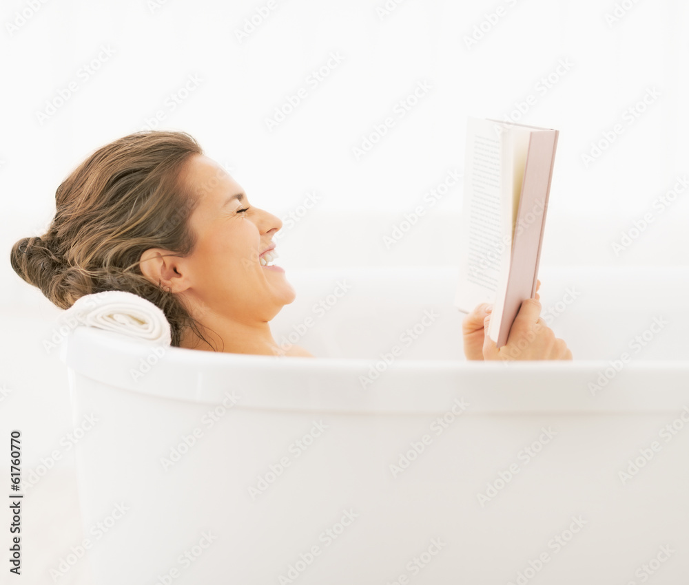 Naklejka premium Smiling young woman in bathtub reading book