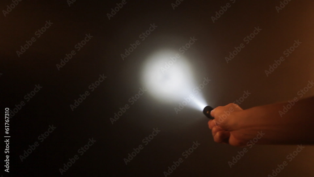 Hand with pocket flashlight looking for something in darkness