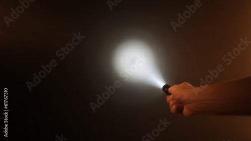 Hand with pocket flashlight looking for something in darkness