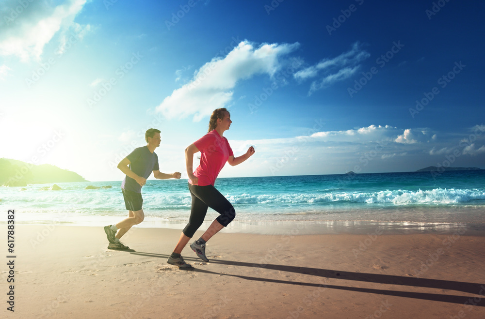 Man and women running on tropical beach at sunset