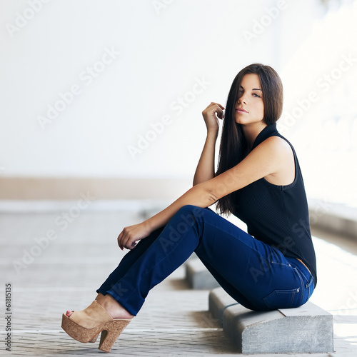 Beautiful girl in jeans sitting in the parking lot
