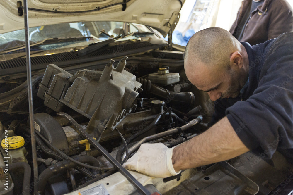 Car mechanic working under a bonnet on a car