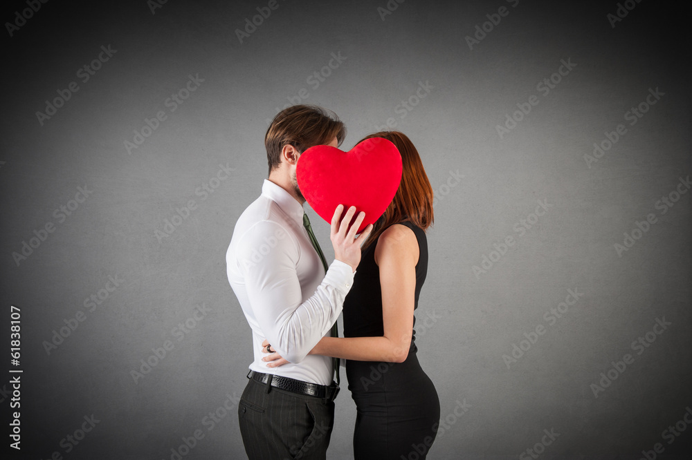 Young couple kissing behind red heart on Valentines Day against Young couple kissing behind red heart on Valentines Day against