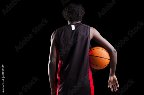 Rear view of a basketball player holding a ball against dark bac