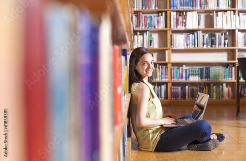 Young smiling student using her laptop in a library