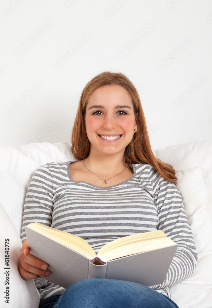 Frau mit Buch auf dem Sofa lacht zur Kamera Frau mit Buch auf dem Sofa lacht zur Kamera