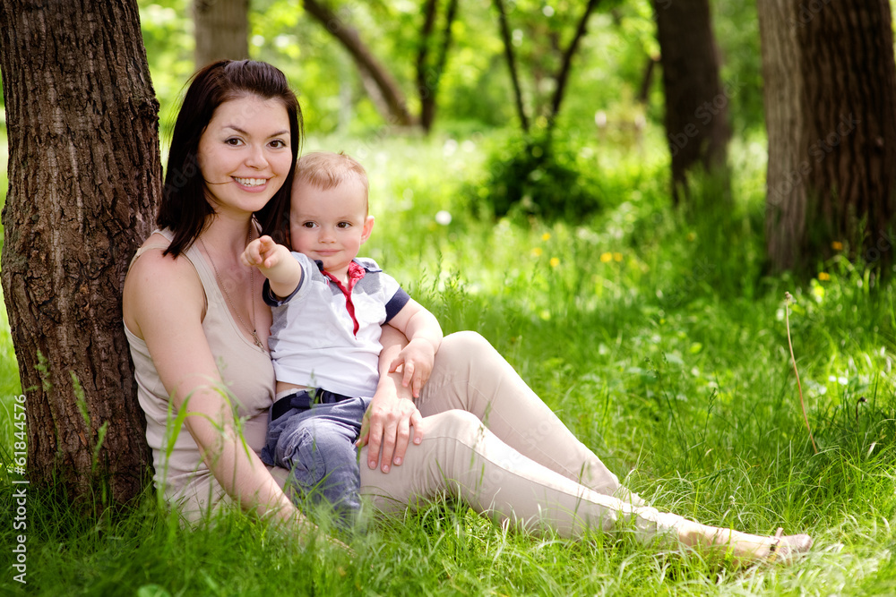 beautiful woman with son sitting down on green grass field beautiful woman with son sitting down on green grass field