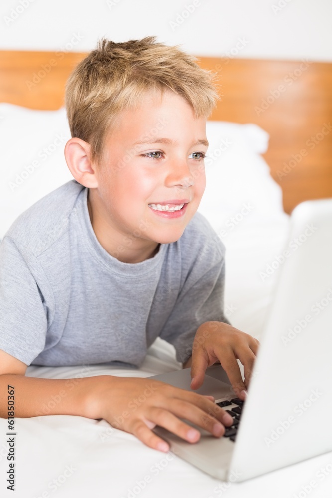 Blonde boy lying on bed using laptop Blonde boy lying on bed using laptop