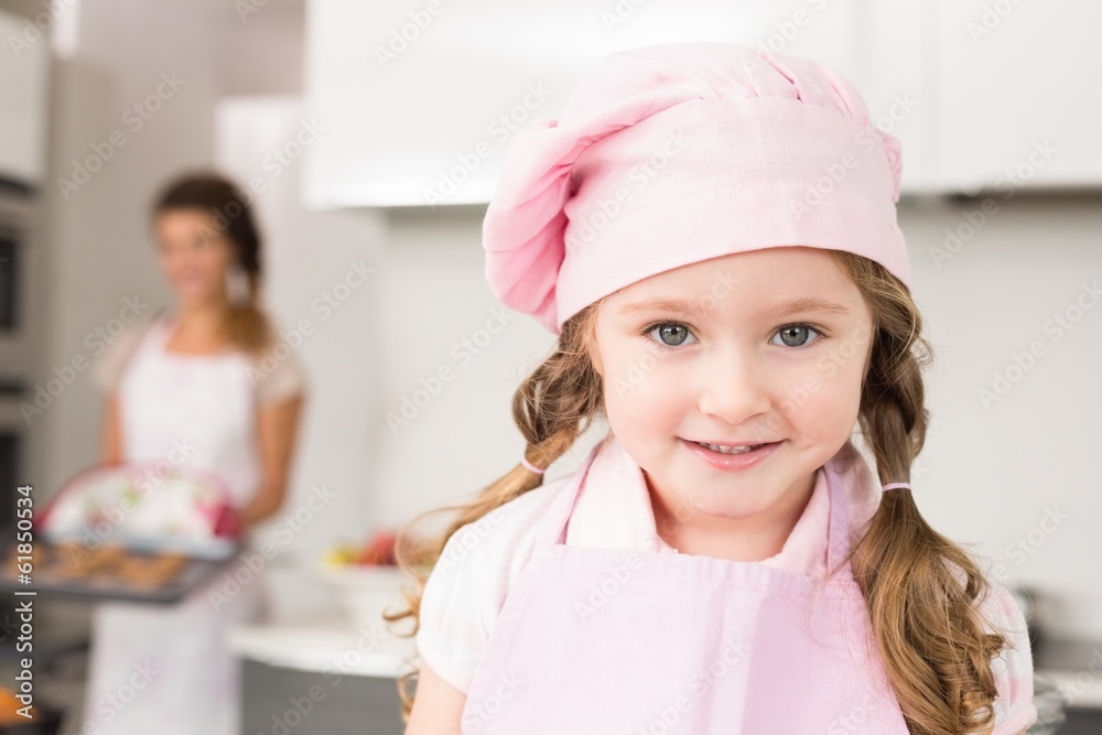 Little girl wearing pink apron and chefs hat smiling at camera Little girl wearing pink apron and chefs hat smiling at camera