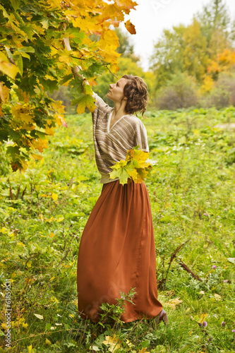 Young beatiful woman collecting autumn maple leaves