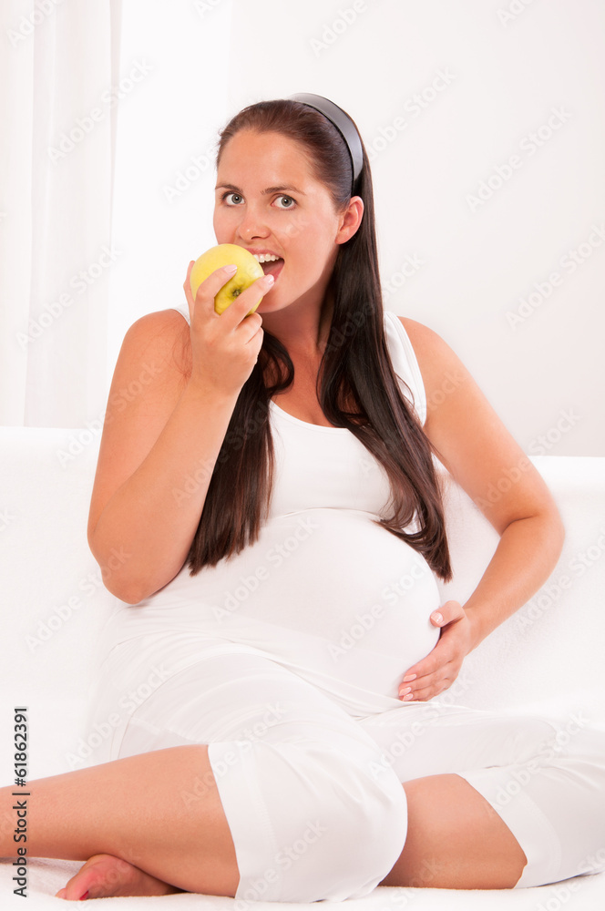 Beautiful pregnant woman on sofa eating an apple Beautiful pregnant woman on sofa eating an apple