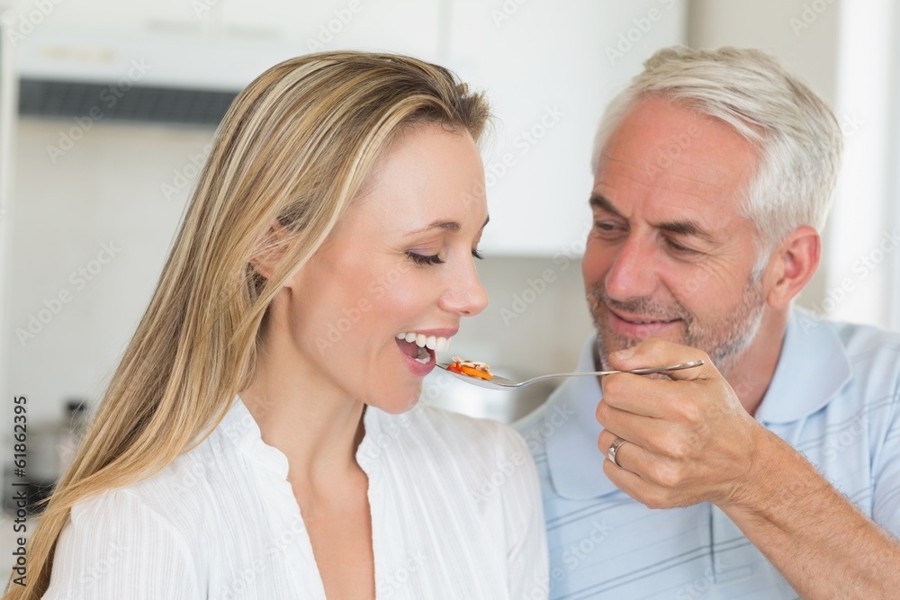 Happy man feeding his partner a spoon of vegetables Happy man feeding his partner a spoon of vegetables