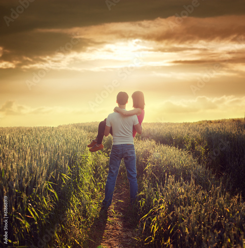 Man Carries Woman at Summer Field in Sunset