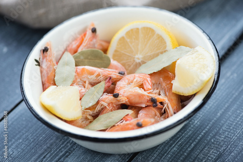 Enameled bowl with boiled shrimps over wooden surface, close-up