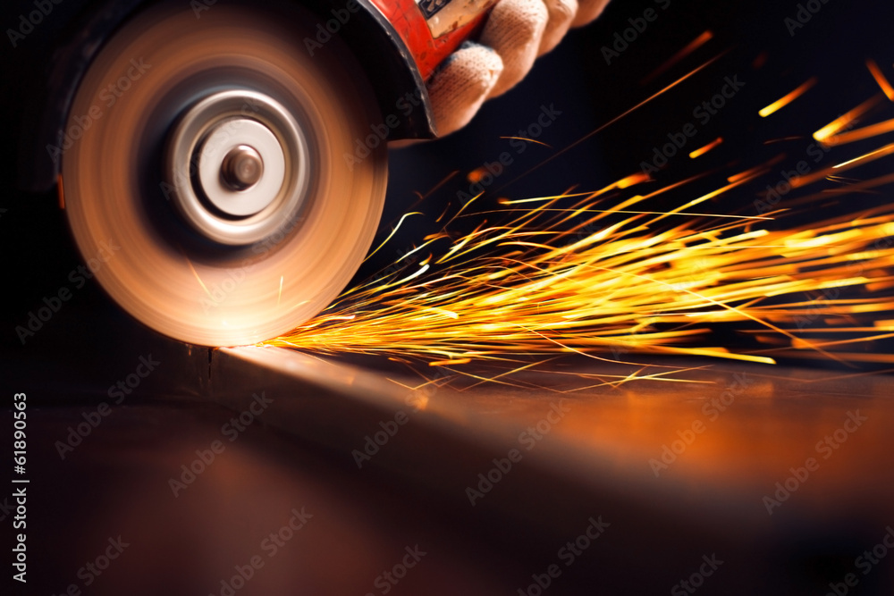Worker cutting metal with grinder. Sparks while grinding iron - obrazy, fototapety, plakaty 