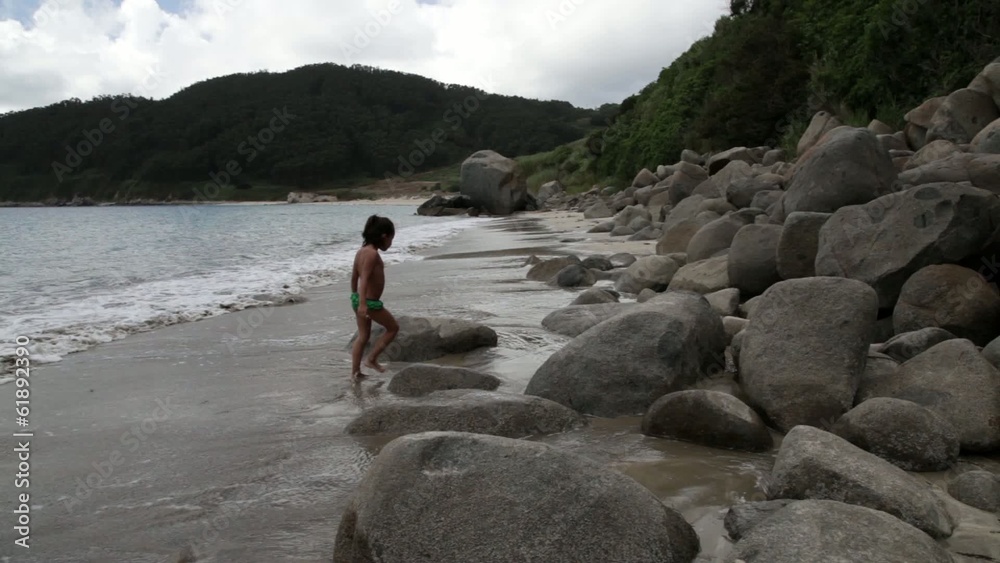 Niña paseando por la playa entre rocas
