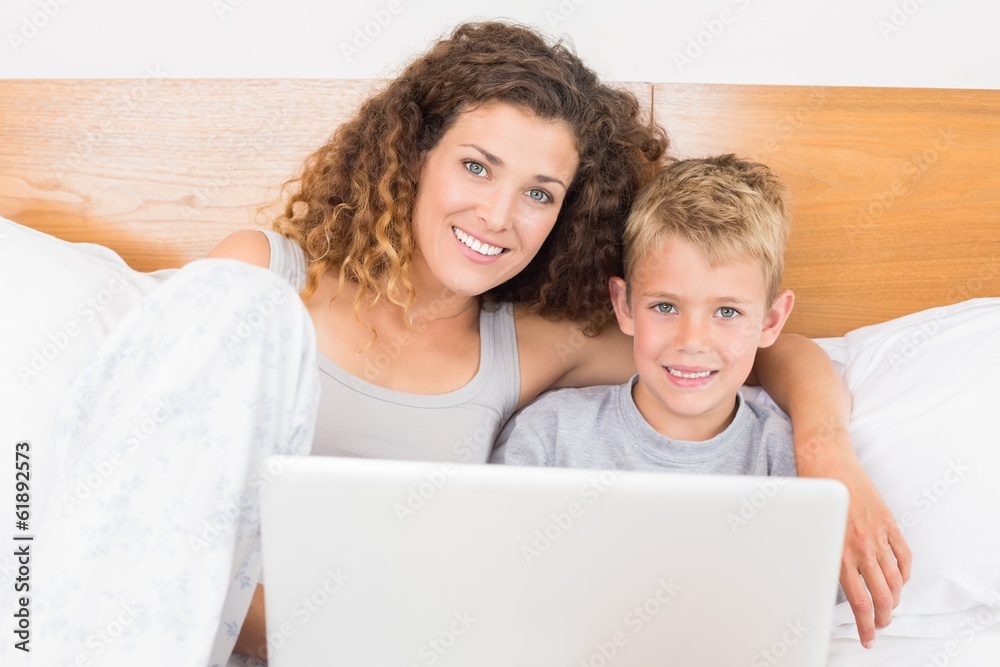 Pretty mother and son sitting on bed using laptop Pretty mother and son sitting on bed using laptop