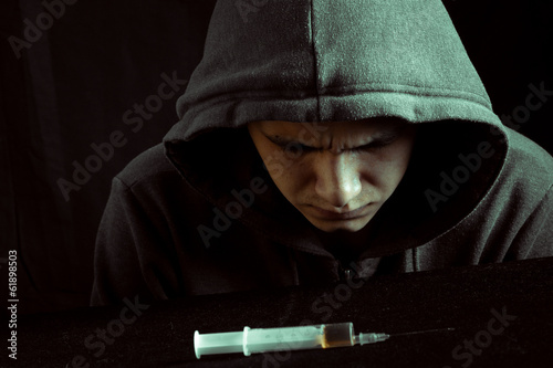 Grunge image of a depressed drug addict looking at a syringe photo