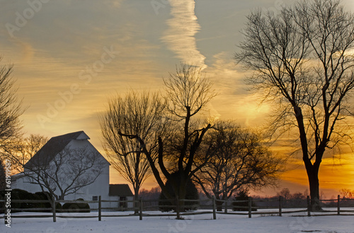 Rural farm barns and trees at sunset in winter with great clouds