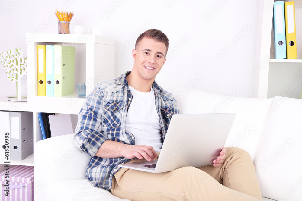 Handsome young man sitting on couch with laptop in room Handsome young man sitting on couch with laptop in room