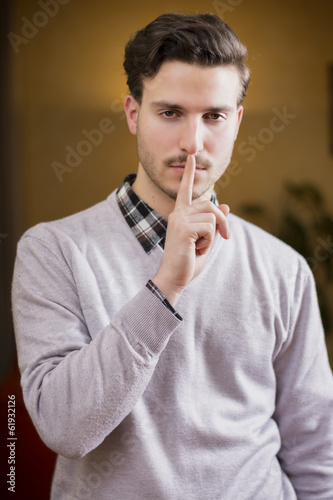 Handsome young man doing Hush sign with finger on lips