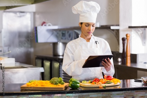 Female chef using digital tablet while cutting vegetables