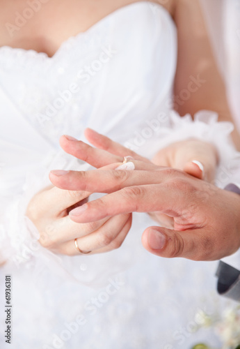 bride in white dress putting wedding ring on grooms finger
