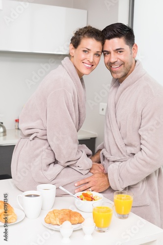 Smiling couple in bathrobes having breakfast together