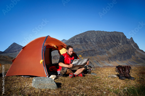 Hiker in front of his Tent, looking Map