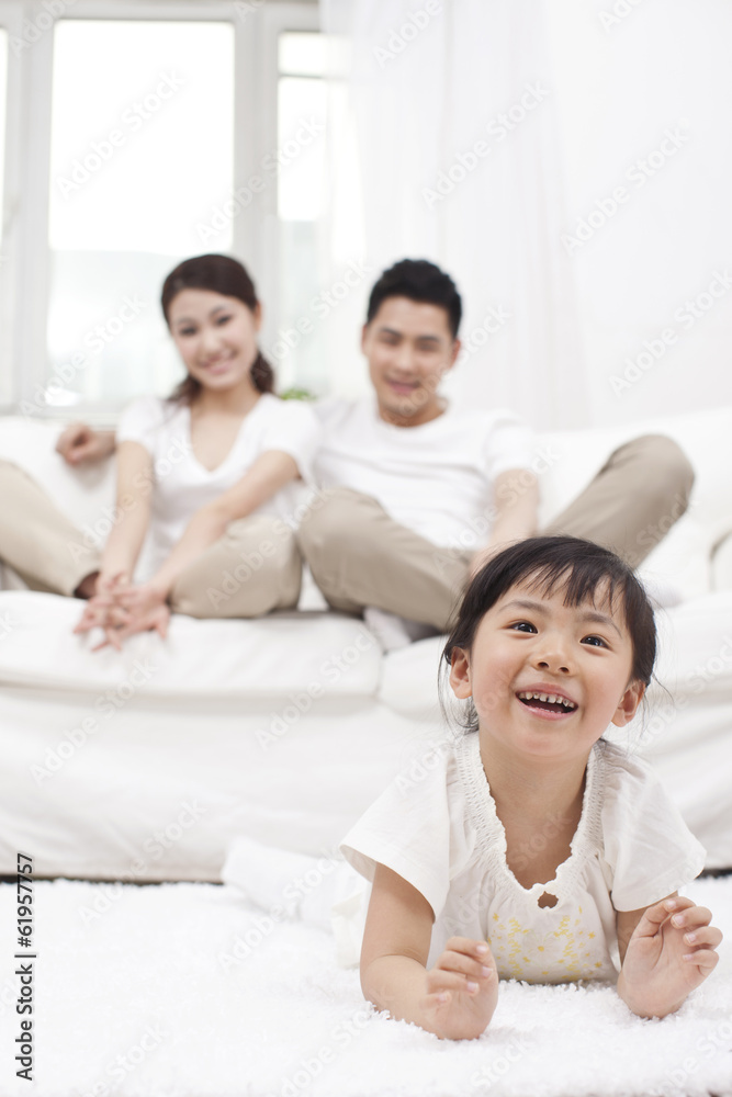 .Young Chinese girl in a living room with parents in the backgro .Young Chinese girl in a living room with parents in the backgro