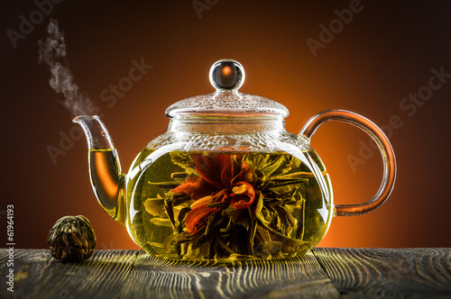 Glass teapot with blooming tea flower on wooden table