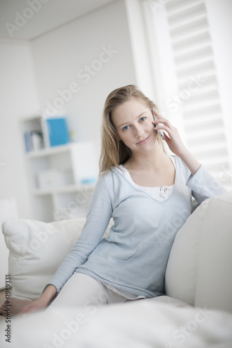 beautiful young woman sitting on a sofa and calling a friend wit