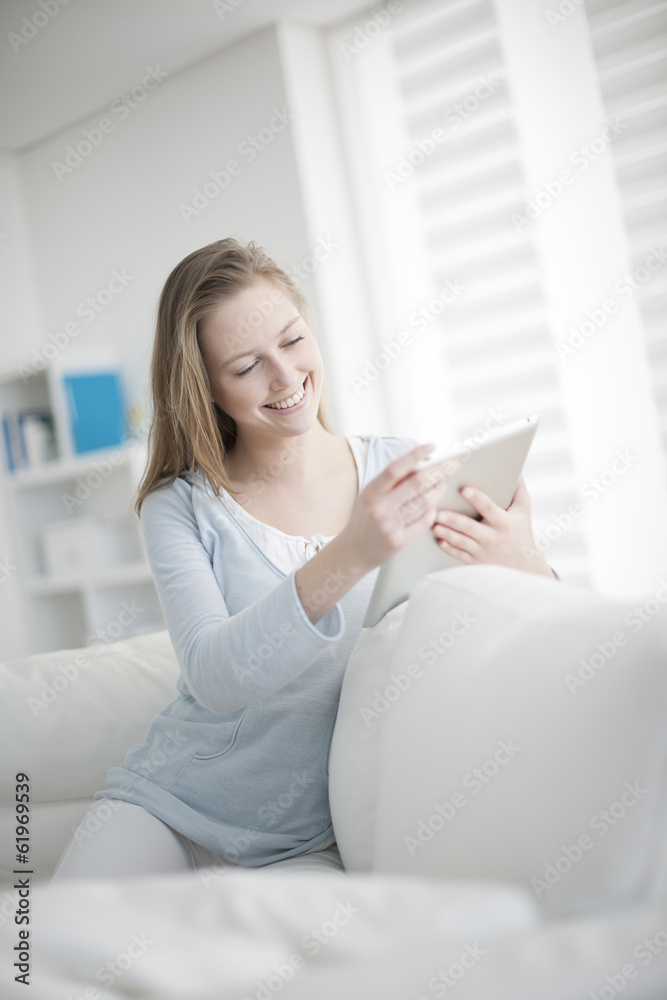 beautiful young woman sitting on a sofa and using a digital tabl