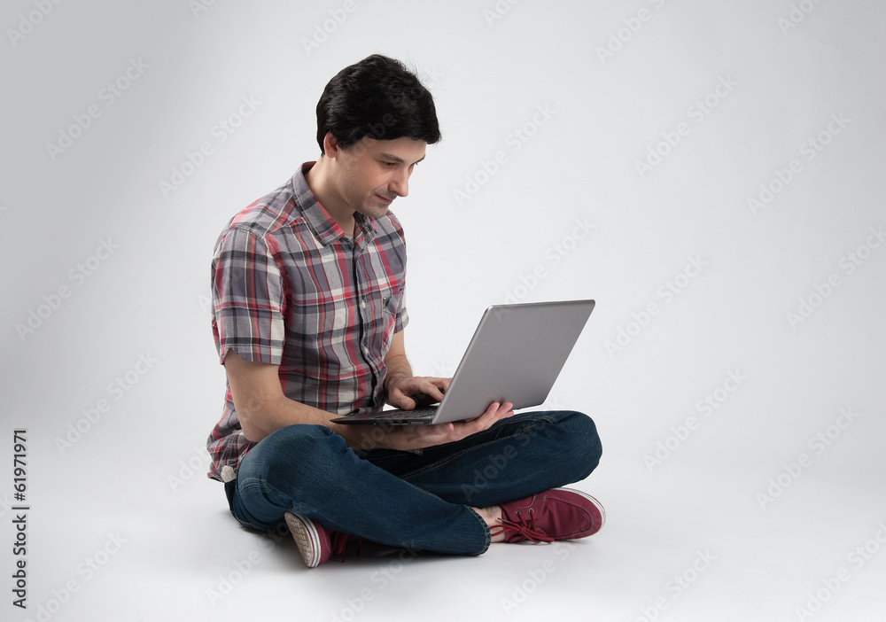 Handsome guy working on a laptop and sitting on the floor Handsome guy working on a laptop and sitting on the floor