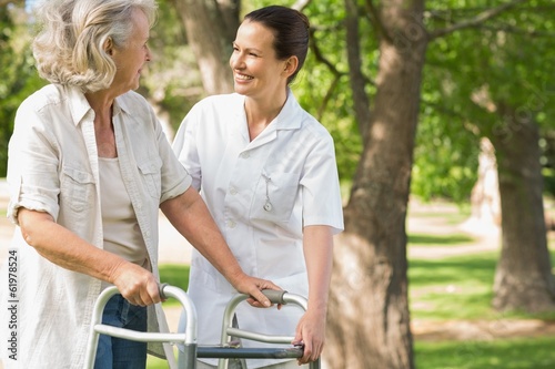 Woman assisting mature female with walker at park