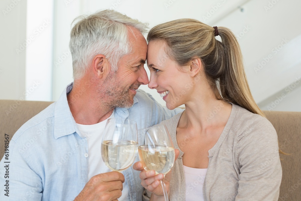 Happy couple sitting on couch toasting with white wine Happy couple sitting on couch toasting with white wine