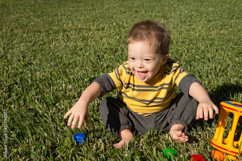 Quadro su tela Laughing Down Syndrome child in grass with toys