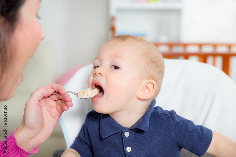 Mother feeding hungry baby in the highchair indoors Mother feeding hungry baby in the highchair indoors
