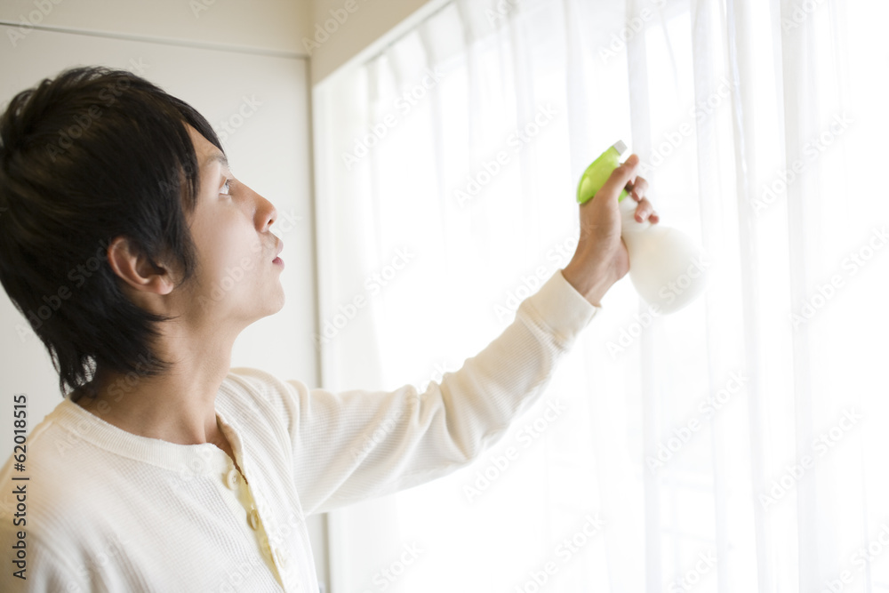 man spraying deodorant spray on curtain