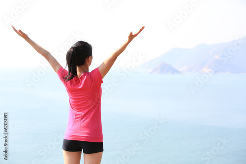  cheering woman hiker open arms at seaside mountain peak
