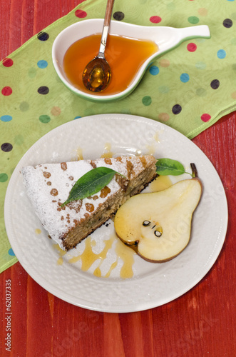 Slice of pear pie with honey on red wooden table