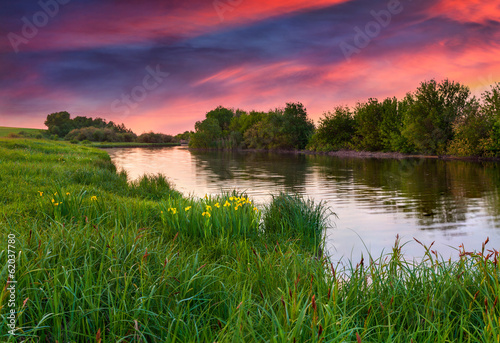 Fototapeta Naklejka Na Ścianę i Meble -  dramatic sunset over flowering meadow by river