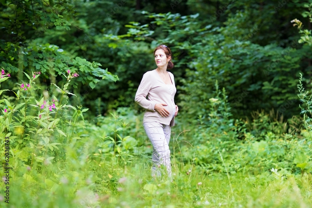 Beautiful young pregnant woman walking in a park Beautiful young pregnant woman walking in a park
