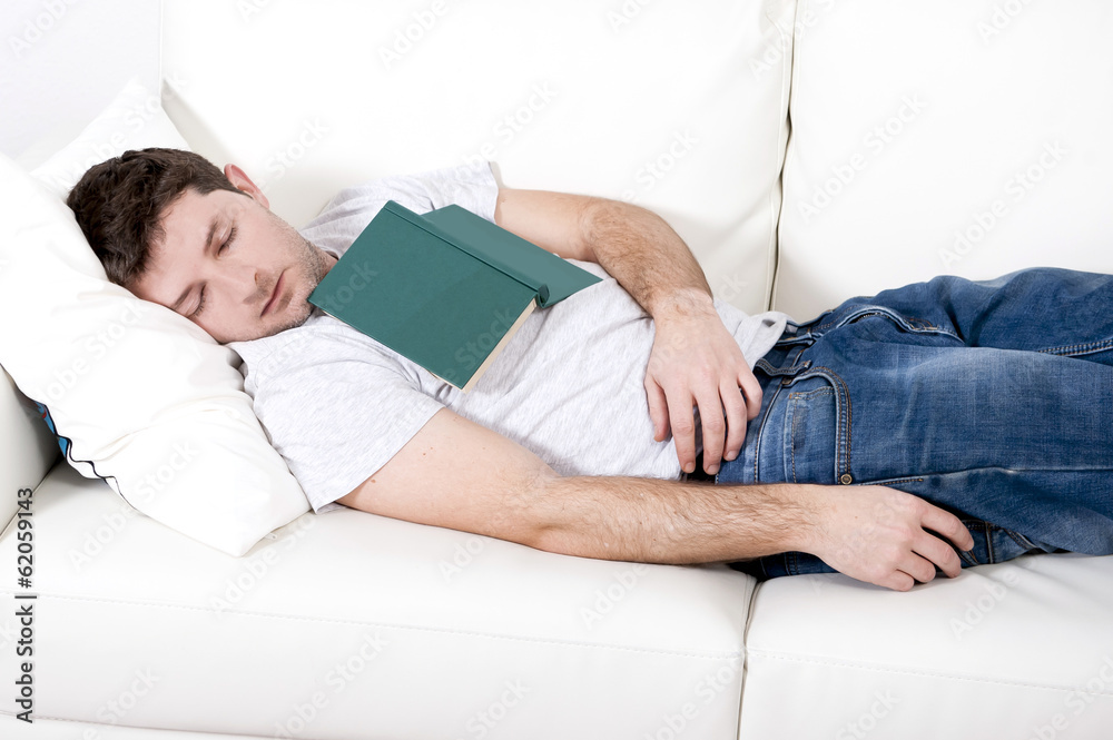 tired young man sleeping on couch with book on lap