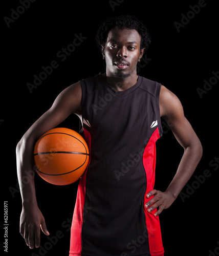 Portrait of a basketball player holding a ball against dark back