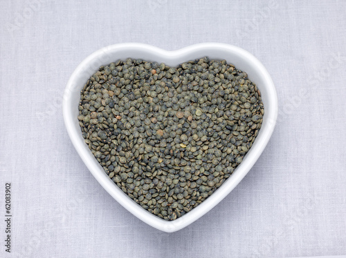 Green lentils in a heart shaped bowl on a woven table cloth