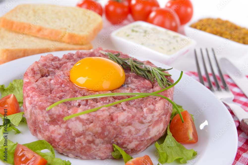 Delicious steak tartare with yolk on plate on table close-up Delicious steak tartare with yolk on plate on table close-up