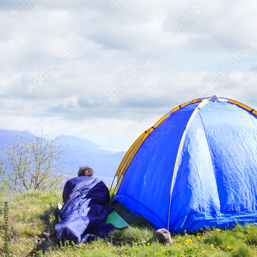 Man lie in sleeping bag near the tent