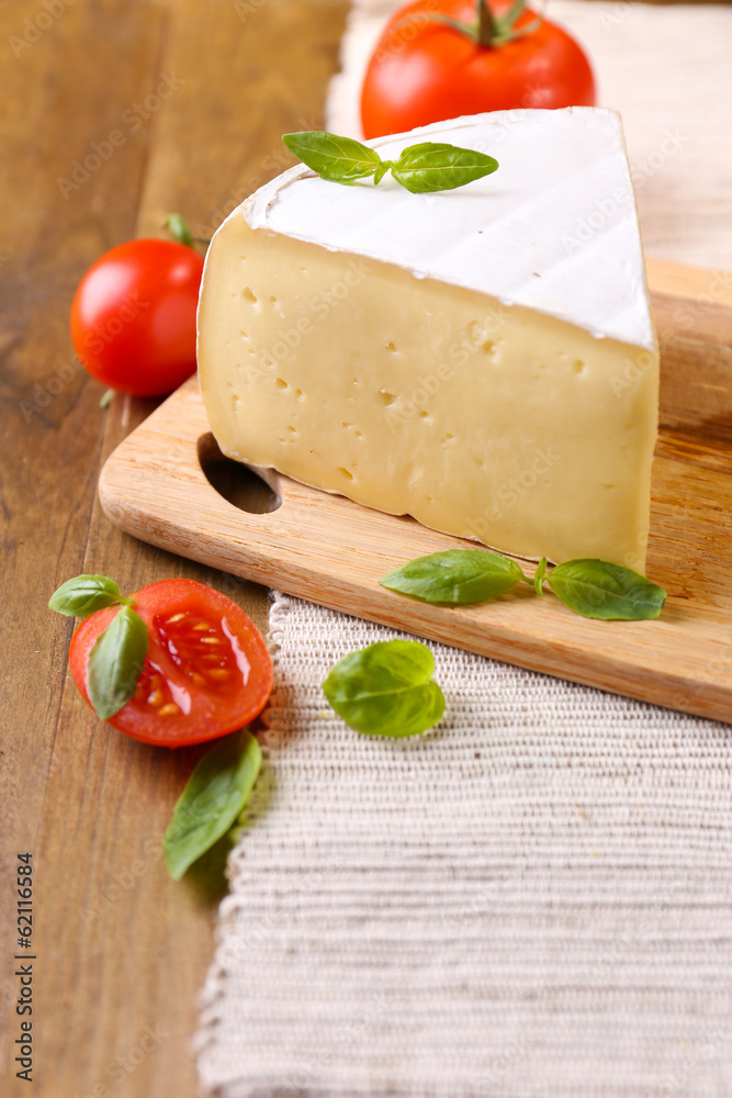Tasty Camembert cheese with tomatoes and basil, on wooden table Tasty Camembert cheese with tomatoes and basil, on wooden table
