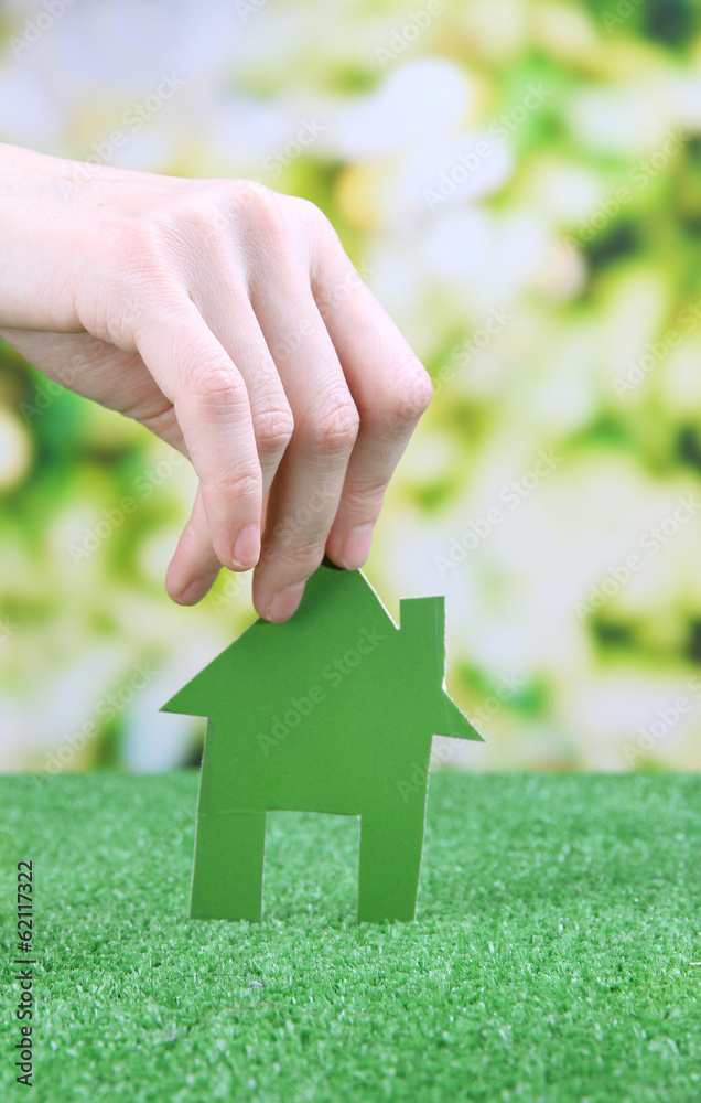 Little paper house in hand on green grass on bright background Little paper house in hand on green grass on bright background